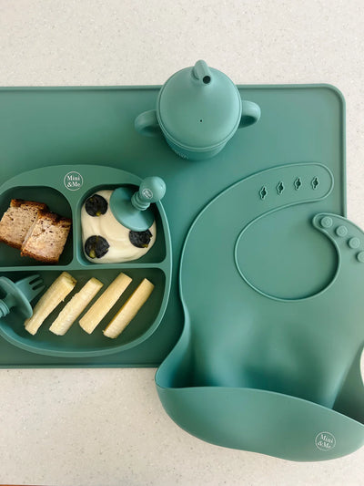 Green children's meal set with tray, bowl, and utensils on a light background