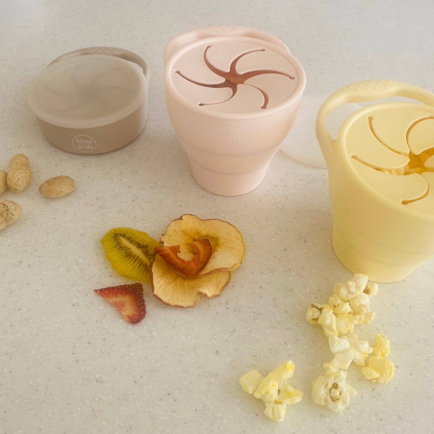 The Mini & Me Snack Cup Collapsible with Lid Almond in almond, ice-blue and kale-green styled beautifully on a shelf in a ...
