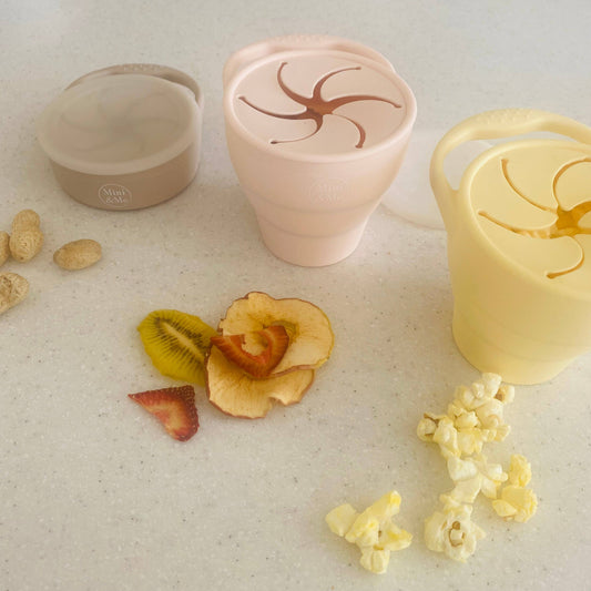 The Mini & Me Snack Cup Collapsible with Lid Almond in almond, ice-blue and kale-green styled beautifully on a shelf in a ...