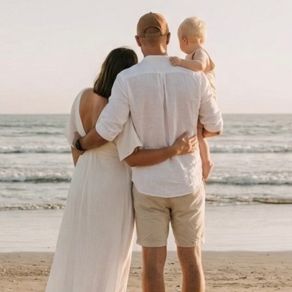 Family of three standing on a beach, looking out at the ocean.