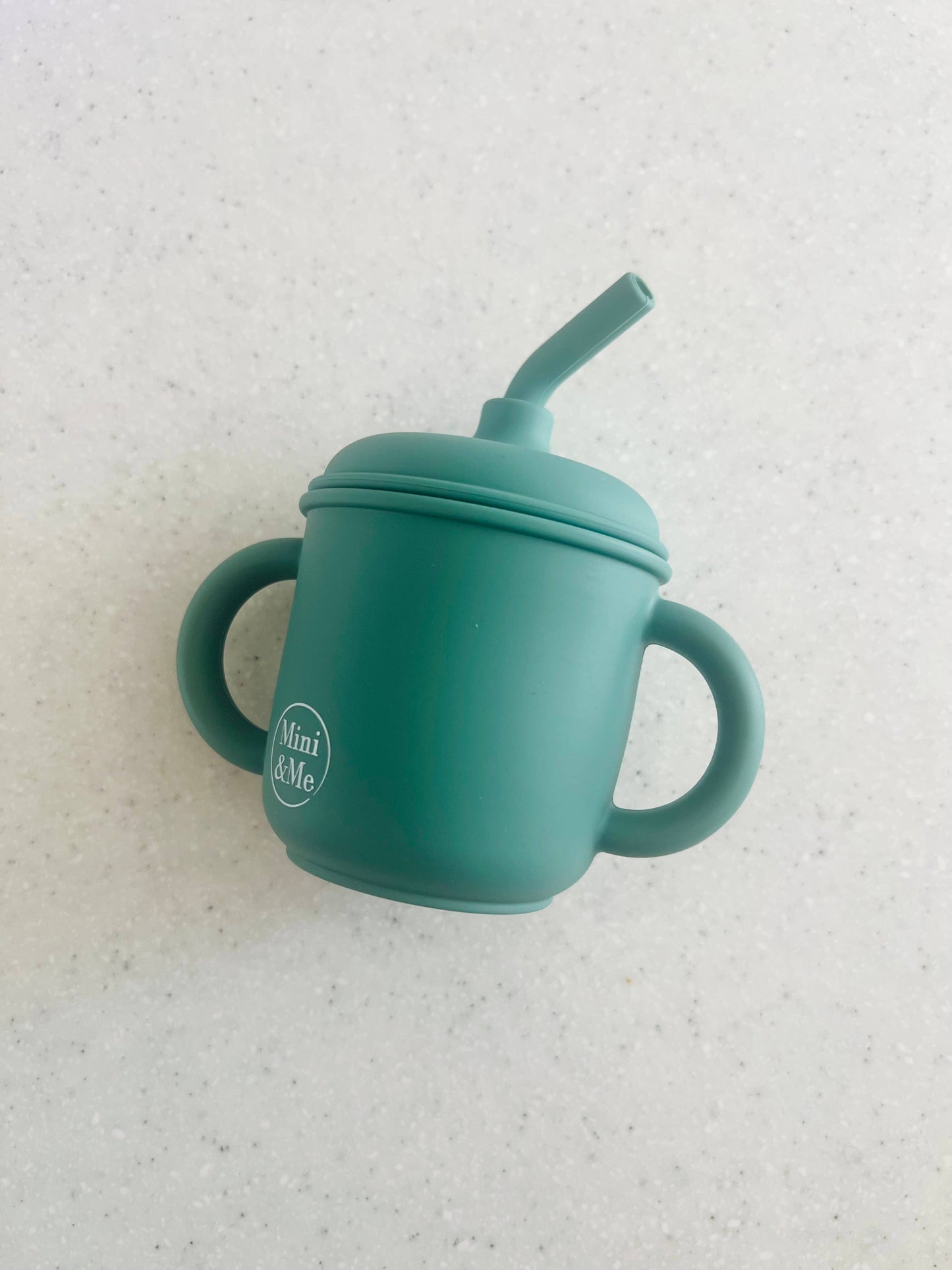 A beautiful lifestyle shot of Mini & Me Transitional Straw Sippy Cup Kale in almond, ice-blue and kale-green by Cuddle Bug...