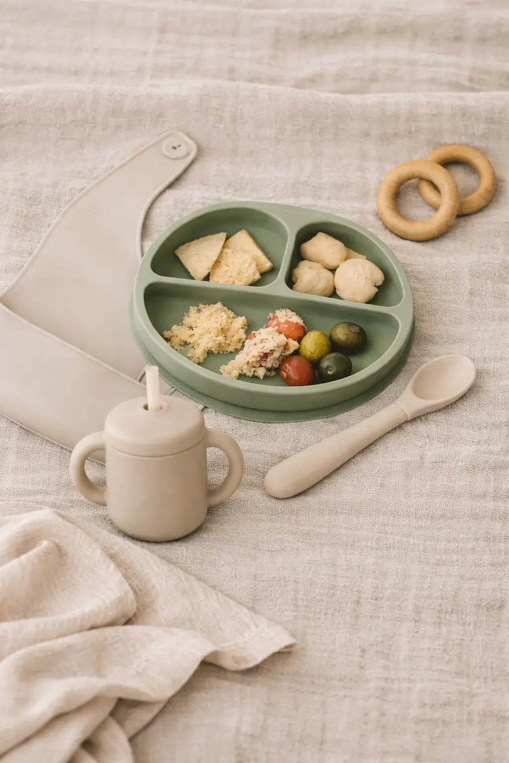 Children's meal set with a green divided plate, cup, spoon, and toys on a beige fabric background