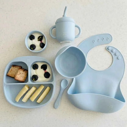 Baby mealtime set with blue tray, bowl, cup, bib, and spoon on a light background