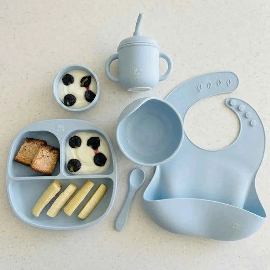 Baby mealtime set with blue tray, bowl, cup, bib, and spoon on a light background