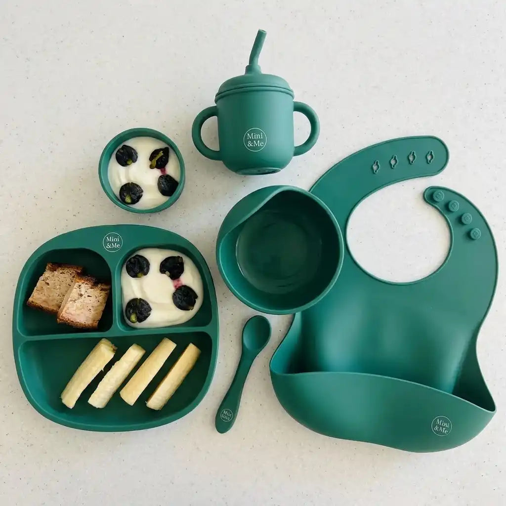 Green children's dining set with bowl, spoon, cup, and bib on a white background