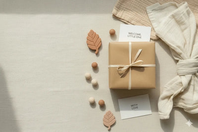 Gift box with ribbon, baby items, and 'Welcome Little One' card on a neutral background