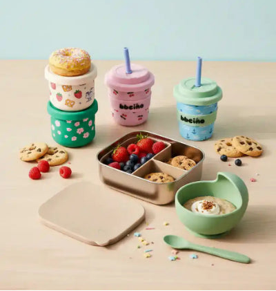 Set of feeding essentials such as sippy cups and stainless steel container on a wooden table. - Tiny Moments co