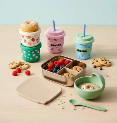 Set of colorful children's feeding essentials including cups, a snack container, and a bowl on a light background.